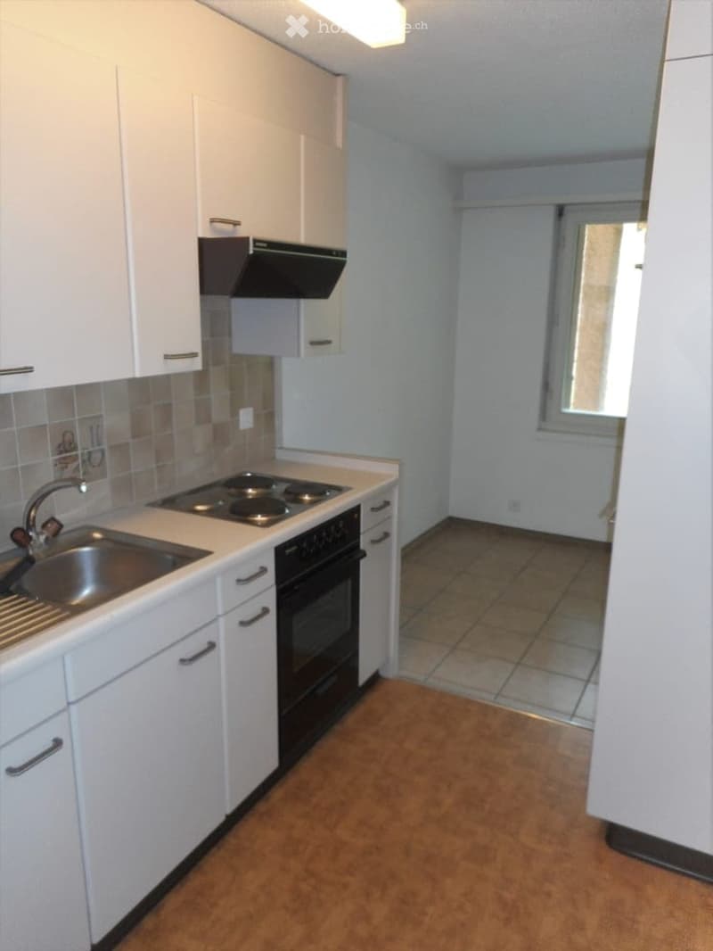 Modern kitchen with white cabinets, stainless steel sink, electric stove, and oven. Light-colored tiled backsplash and wooden flooring.
