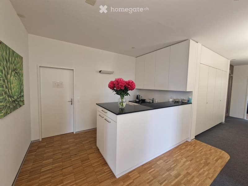 Modern kitchen with white cabinets, black countertop, and a vase of red flowers on the counter.