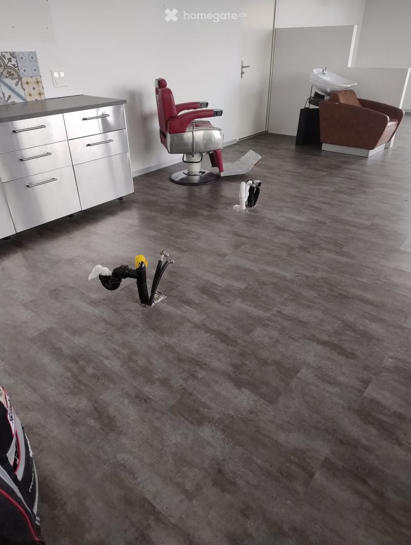 Modern salon with grey flooring, white walls, red and brown chairs, a sink, and a cabinet.