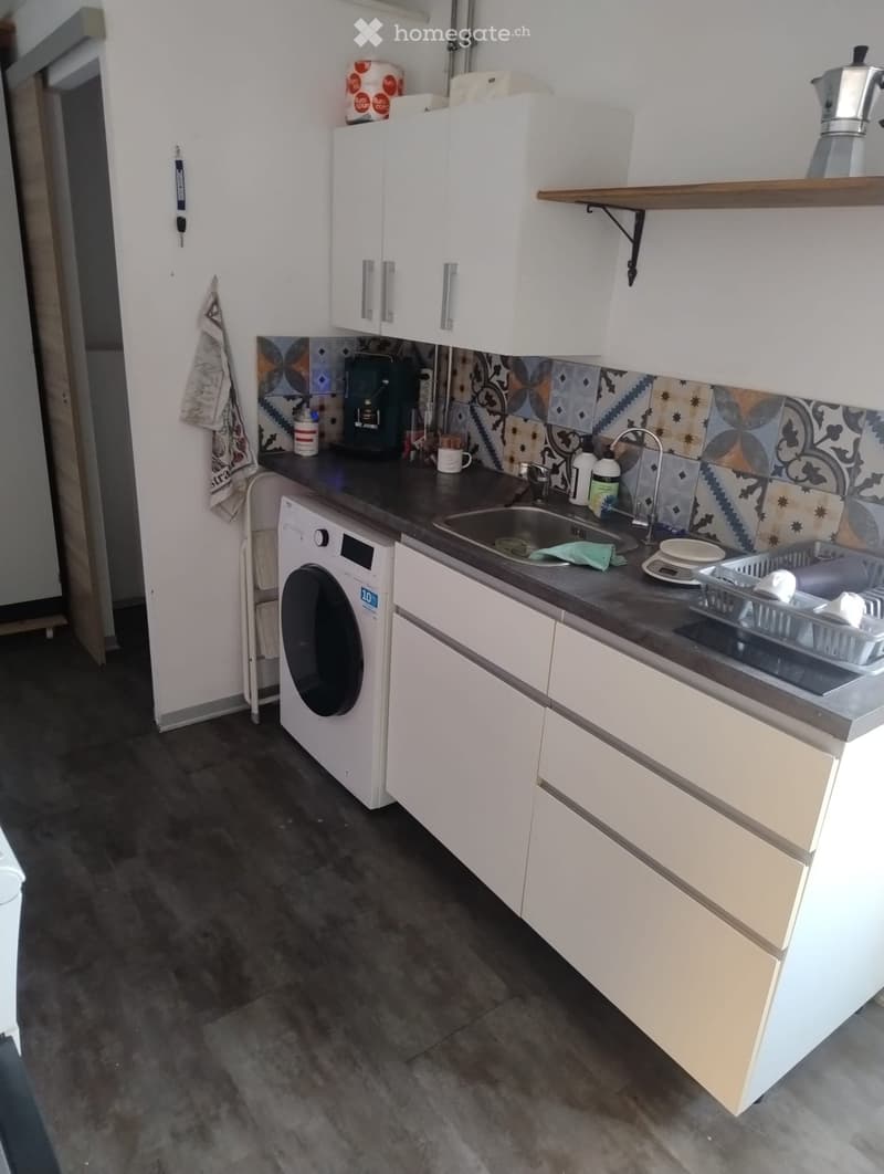 Modern kitchen with white cabinets, dark countertops, and a sink area. Includes a coffee maker, washing machine, and various small appliances.