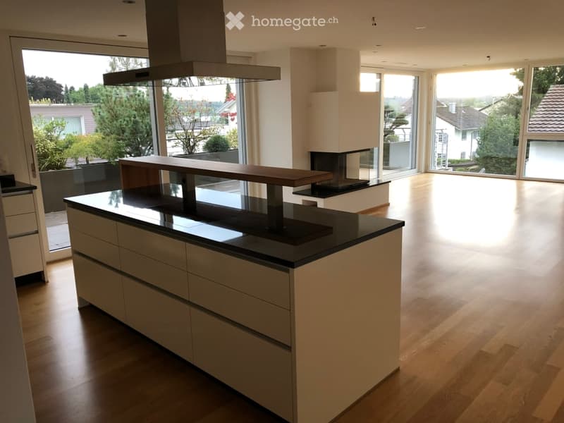 Modern kitchen with a central island, black countertop, and a range hood. Large windows provide natural light and a view of the outdoor area.