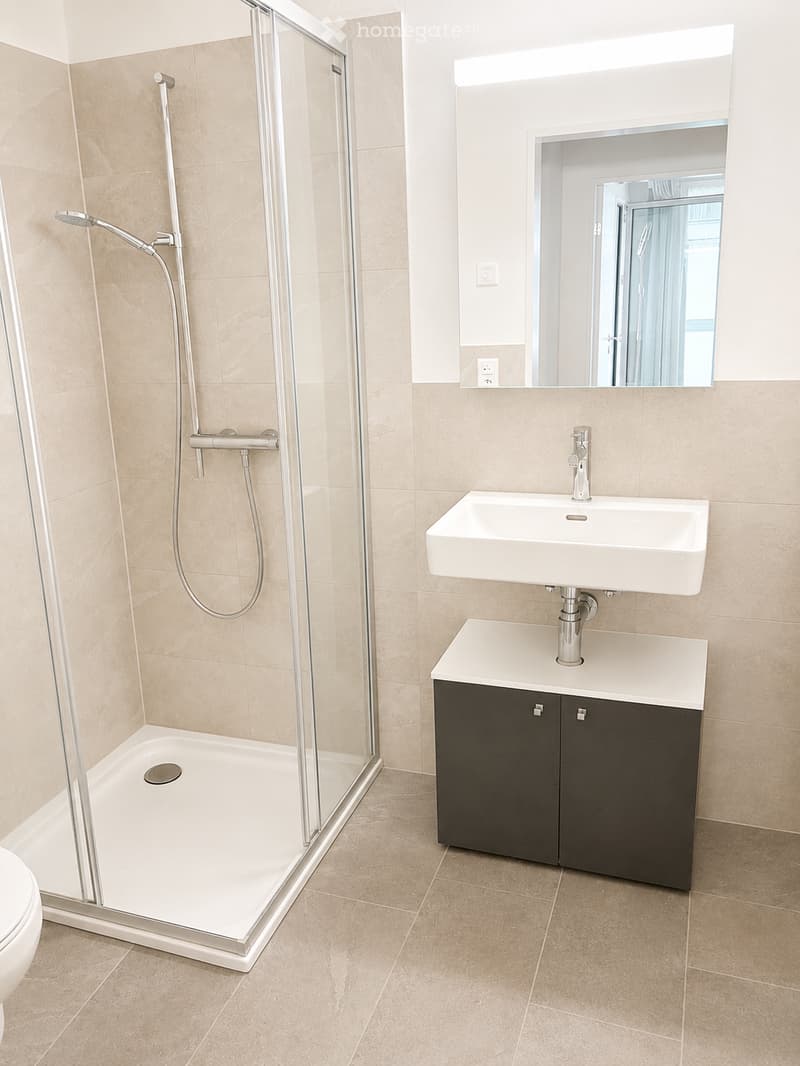 Modern bathroom with beige tiles, a white shower stall with glass enclosure, a white sink with a modern faucet, a dark wooden cabinet, and a large mirror above the sink.