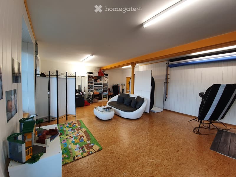 A spacious, well-lit room with wooden flooring, a modern white sofa, a coffee table, shelves, a screen, and a small play area with toys and a rug.