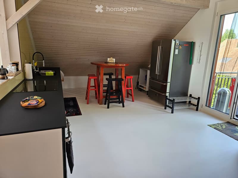 Modern kitchen with wooden ceiling, black countertops, stainless steel refrigerator, round wooden table with red stools, sink, and various kitchen items.