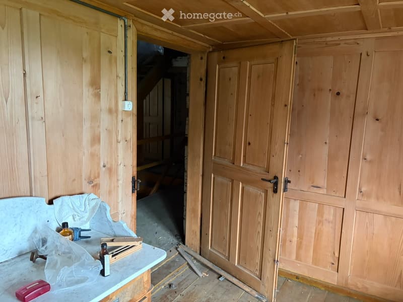 Empty room with wooden walls and doors, exposed wooden beams on the ceiling, and a small table with tools and materials.