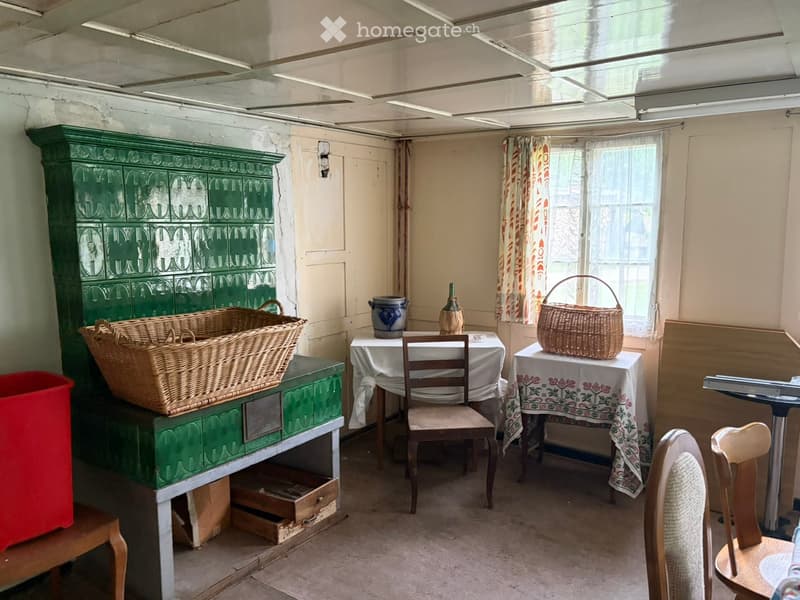 A furnished room with a green painted cabinet, a wooden chair, a small table with a white tablecloth, and various baskets and items on the cabinet and table.
