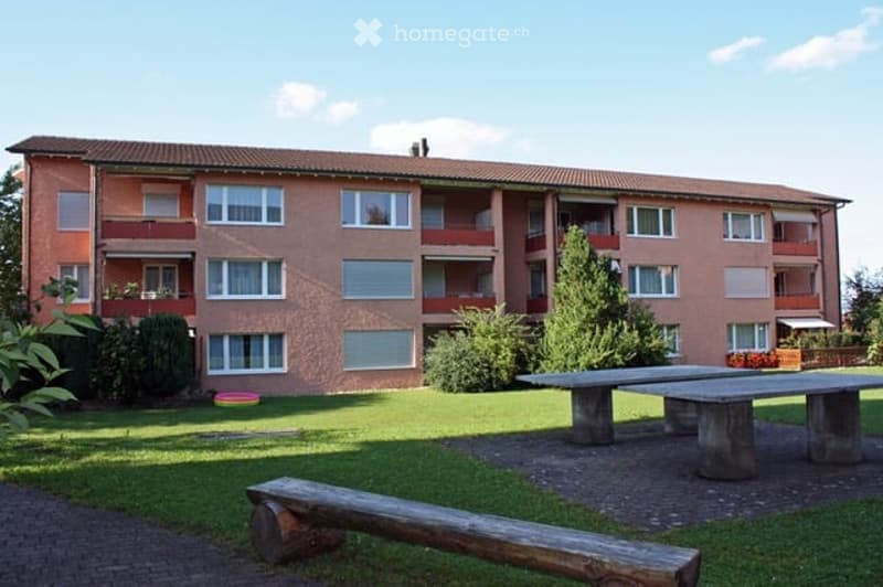 3 story apartment building, brown exterior, multiple windows, balcony, outdoor seating area, green lawn