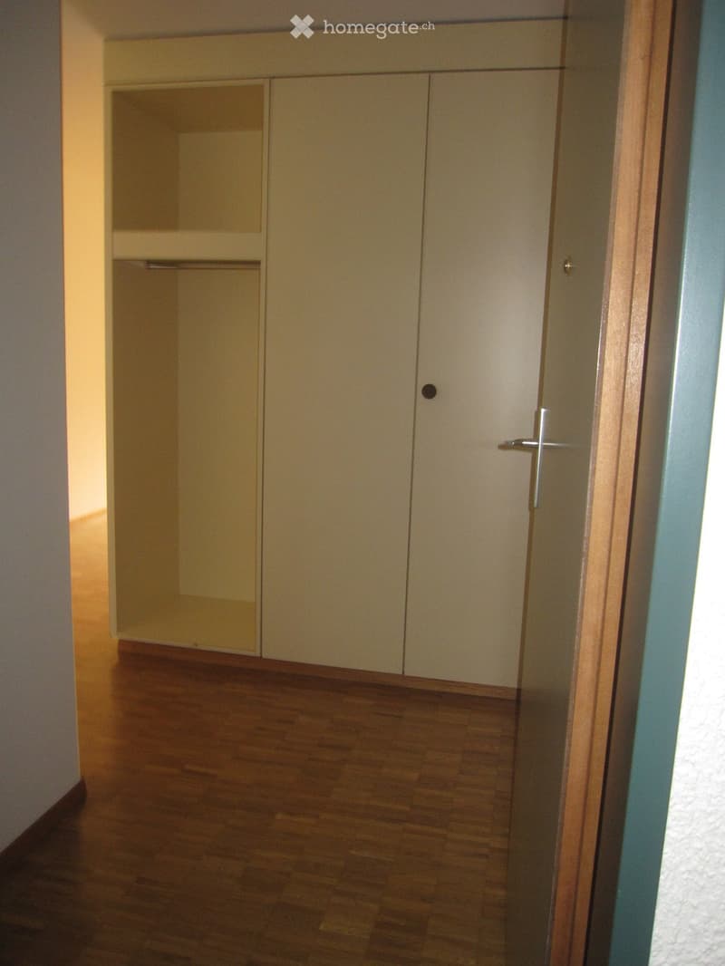 Empty room with wooden floor, white wardrobe, and open door