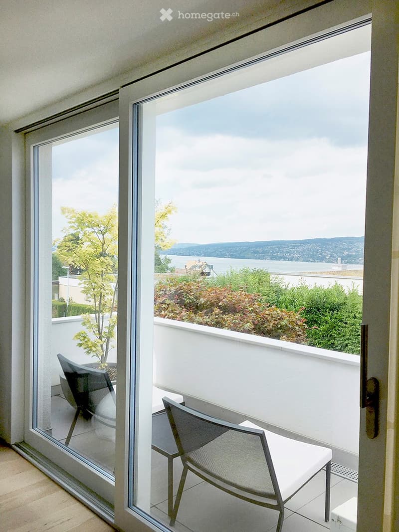 Balcony with modern sliding glass doors, offering a scenic view of a body of water and distant hills, furnished with two contemporary chairs.