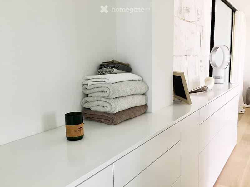 Modern bathroom with white vanity, large mirror, neatly stacked towels, and decorative candle on the counter.