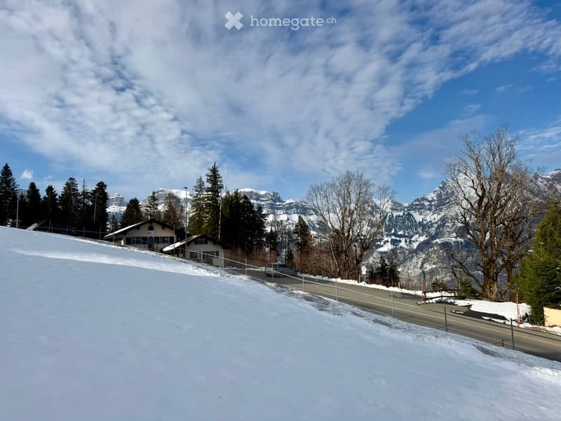 Snowy landscape with a road, houses, and mountains in the background