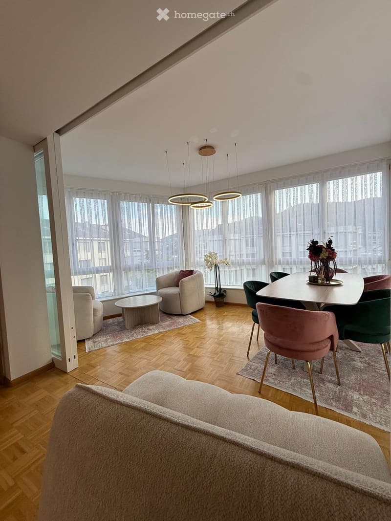 Modern living and dining area with wooden flooring, large windows, and contemporary furniture including a sofa, chairs, coffee table, and dining table.