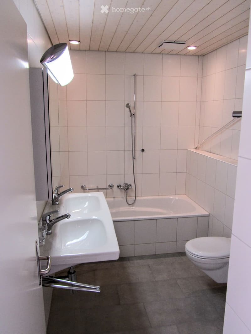 Modern bathroom with a white sink, bathtub, toilet, and showerhead. Features tiled walls and a sleek design.