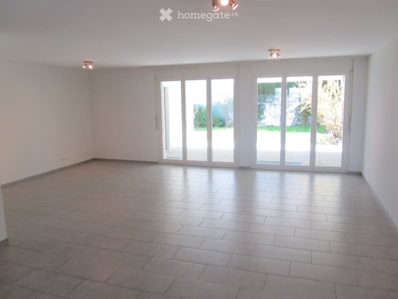 Empty room with tiled floor, white walls, large sliding glass doors leading to an outdoor area, and recessed lighting.