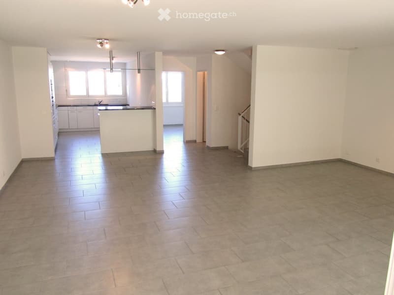 Empty room with tiled floor, white walls, and a kitchen area visible in the background. No furniture or equipment present.