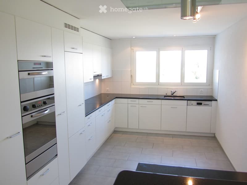 Modern kitchen with white cabinets, stainless steel appliances, black countertops, and tiled flooring.