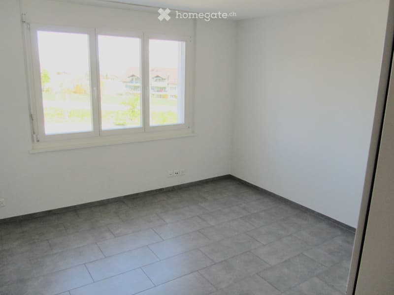 Empty room with tiled floor and large windows offering a view of the outside area.