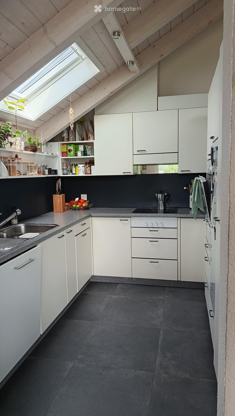 Modern kitchen with white cabinets, dark countertops, and a stainless steel sink. Features include a built-in oven, refrigerator, and various kitchen items on the counter and shelves.