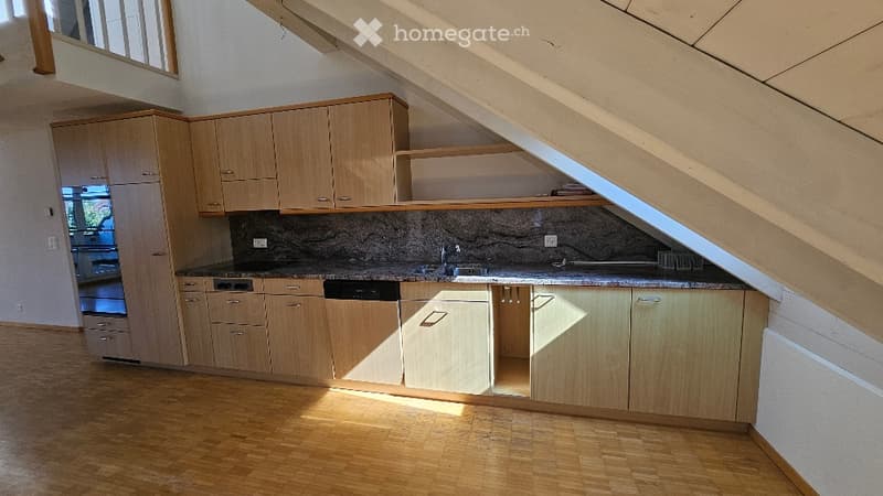 Modern kitchen with light wooden cabinets, granite countertop, and built-in appliances including a dishwasher. The space features a slanted ceiling typical of an attic conversion.