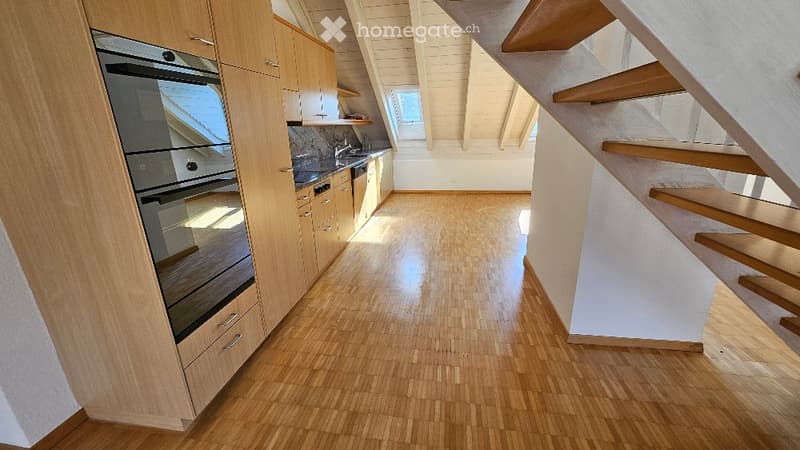 Modern kitchen with light wooden cabinets, stainless steel appliances, and a polished wooden floor. The space is bright with natural light from skylights.