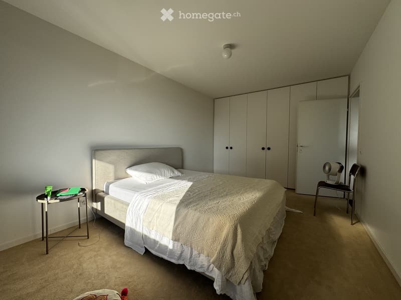 Bedroom with a neatly made bed, nightstand, chair, fan, and built-in wardrobe.
