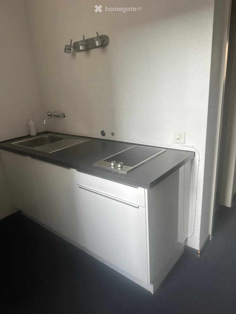 White kitchen cabinets, dark countertop, integrated dishwasher, induction cooktop, single sink with faucet, open wall socket