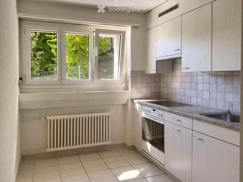 Modern kitchen with white cabinets, granite countertop, stainless steel oven, and sink. Large window with three panes offers natural light.