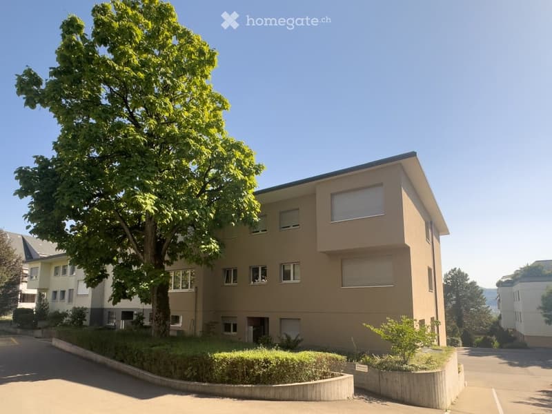 A modern, multi-story residential building with beige walls, multiple windows, and a tree in front.