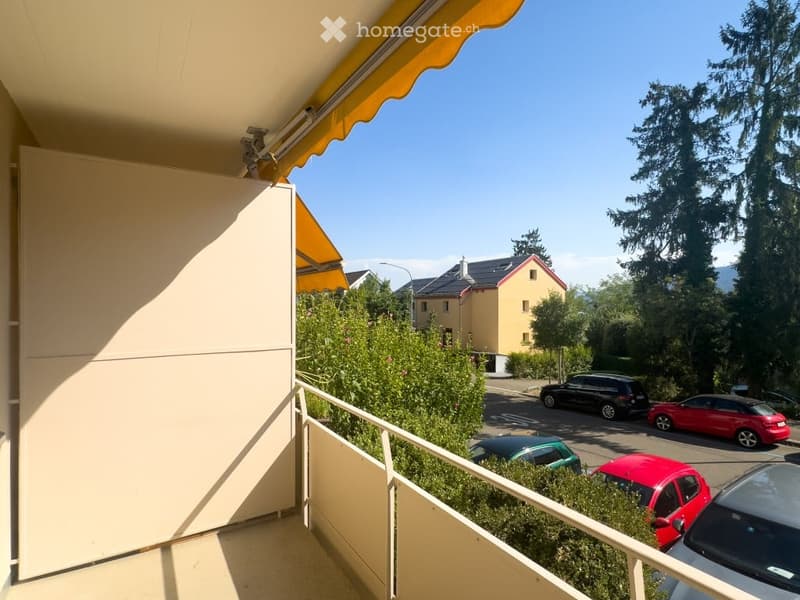 Balcony with yellow awning, metal railing, and view of a parking lot with several cars and surrounding residential buildings.