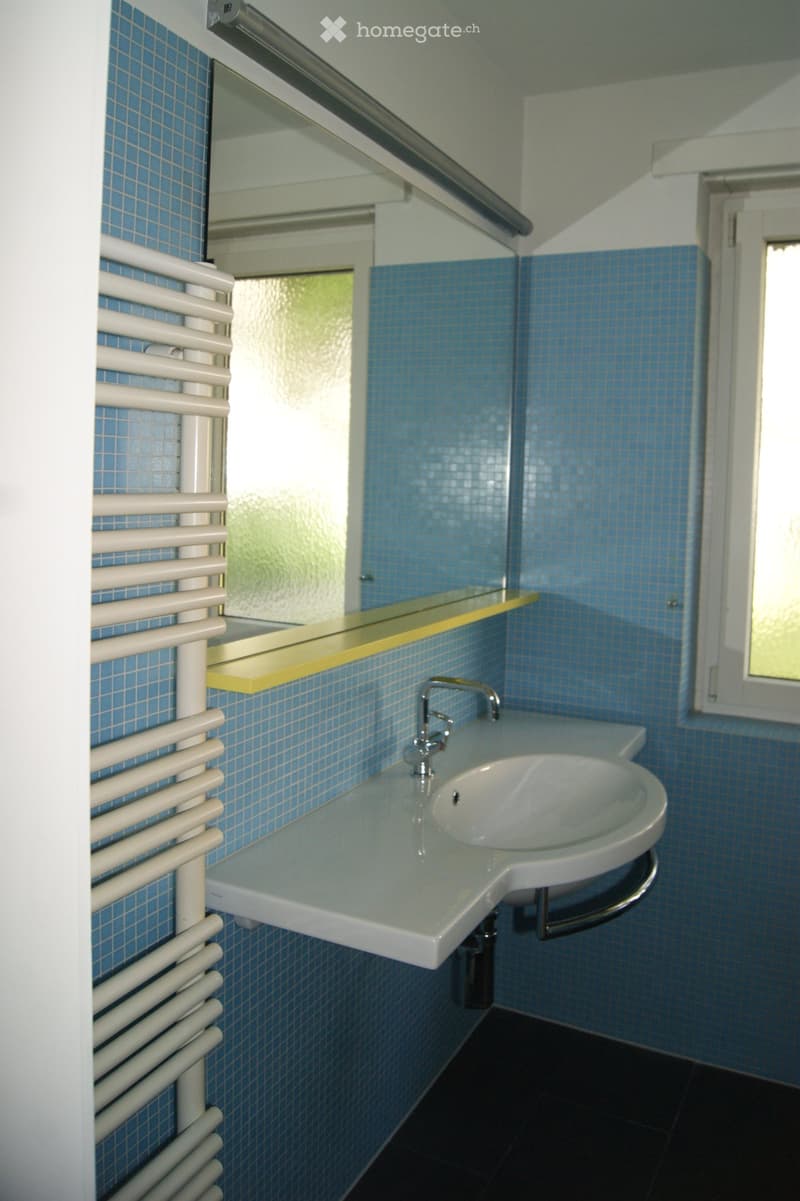 Bathroom with blue tiled walls, a white sink with a modern faucet, a radiator, a mirror, and a yellow shelf above the sink.