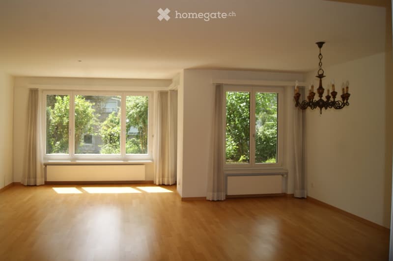 Empty room with wooden flooring, large windows with curtains, radiators, and a chandelier hanging from the ceiling.