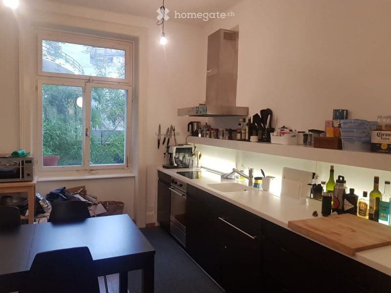 Modern kitchen with dark cabinets, white countertops, stainless steel appliances, and a window overlooking greenery. Includes a sink, oven, microwave, and various kitchen items on the counter.