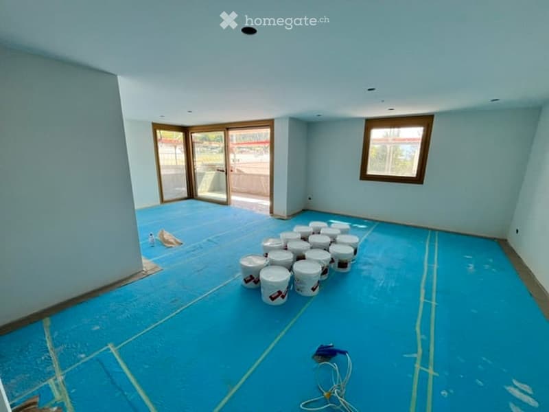 Empty room with light blue walls and a blue floor, featuring a large window and a set of glass doors leading outside. Several white buckets are placed on the floor.