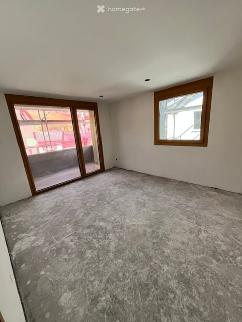 Empty room with bare walls, concrete floor, large sliding glass door, and a small window with wooden frame.