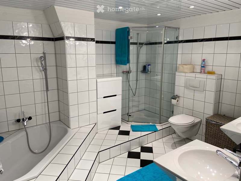 Modern bathroom with white tiles, black accents, bathtub, toilet, sink, glass-enclosed shower, and storage cabinet.