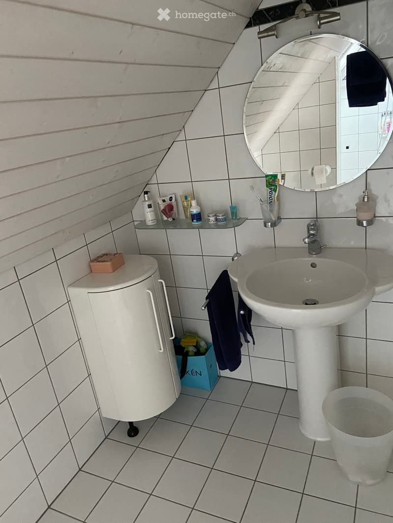 Modern bathroom with white tiles, a sink, a mirror, a toilet, and a cabinet. The sink has a faucet and a toothbrush holder, and there is a towel hanging on the side.