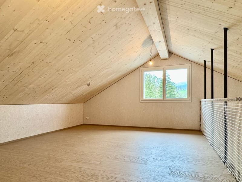 Empty attic space with wooden walls, ceiling, and floor, featuring a large window with a scenic view of trees and mountains.