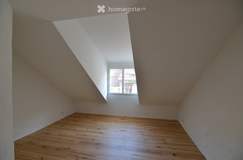 Empty attic room with wooden flooring, white walls, and a skylight window. The room is completely unfurnished with no visible furniture or equipment.