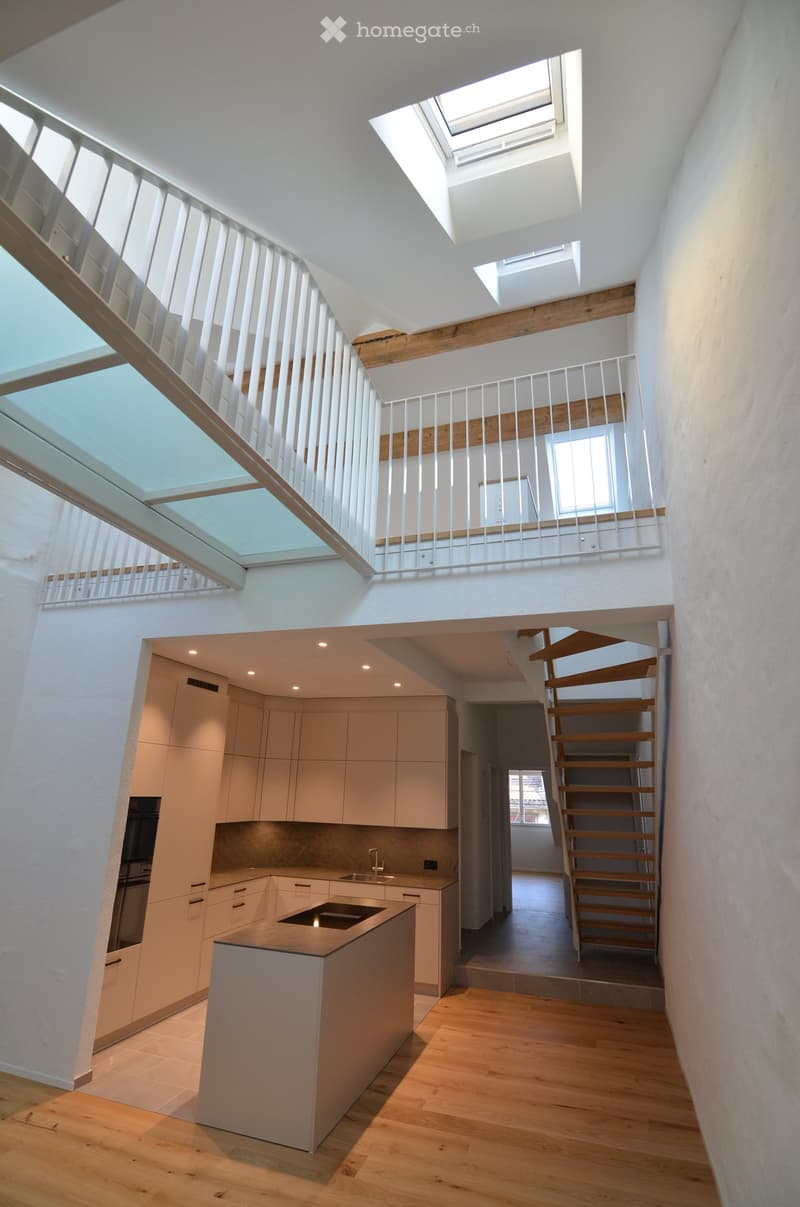 Modern kitchen with light-colored cabinets, a central island, and a staircase leading to an upper level with skylights.