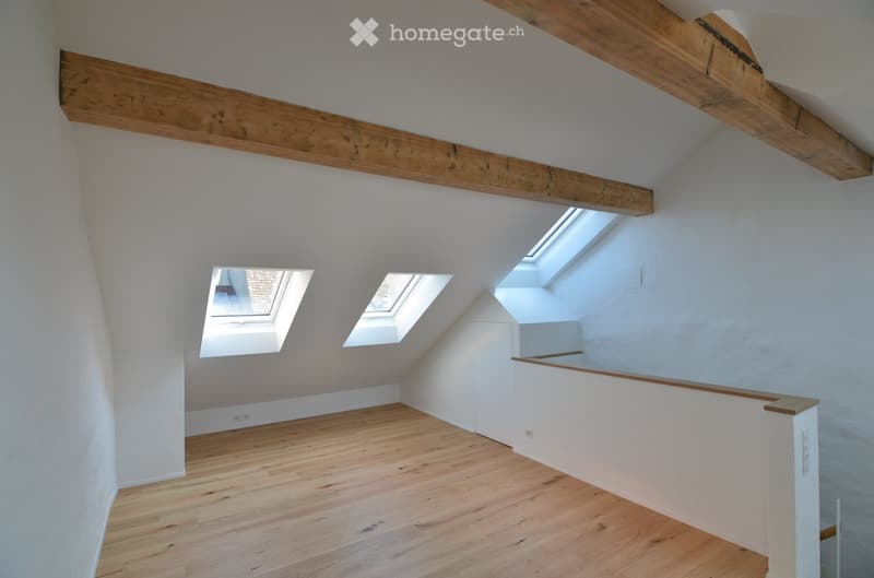 Empty attic room with wooden floor, exposed wooden beams, and three skylight windows.