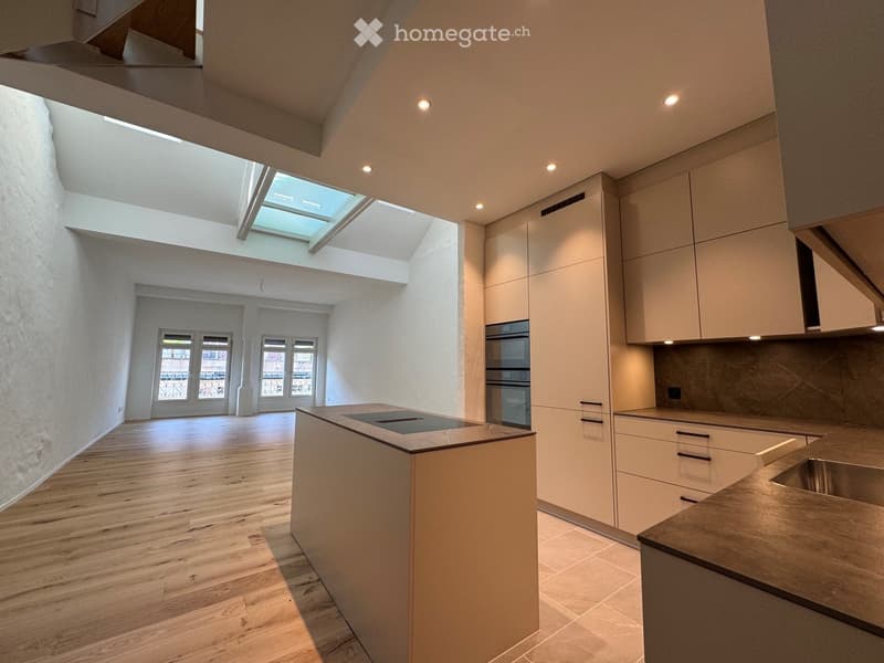 Modern kitchen with light wood flooring, white cabinets, stainless steel appliances, and a central island with a built-in stovetop.