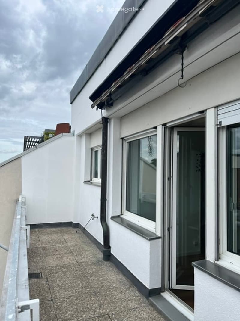 Roof terrace with grey tiled flooring, white walls, large sliding glass door, and a small window. The roof has a low parapet and a visible pipe running along the edge.