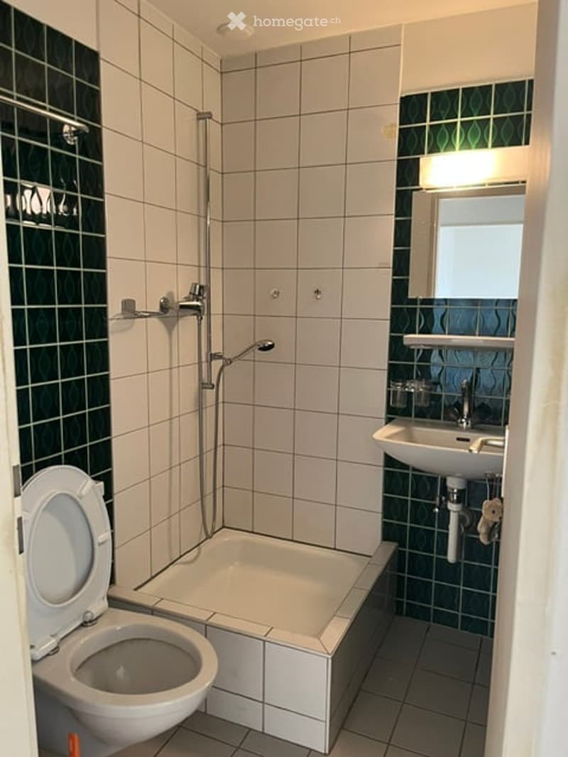 Modern bathroom with white tiles, a bathtub, toilet, sink, and a shower area with a glass door.