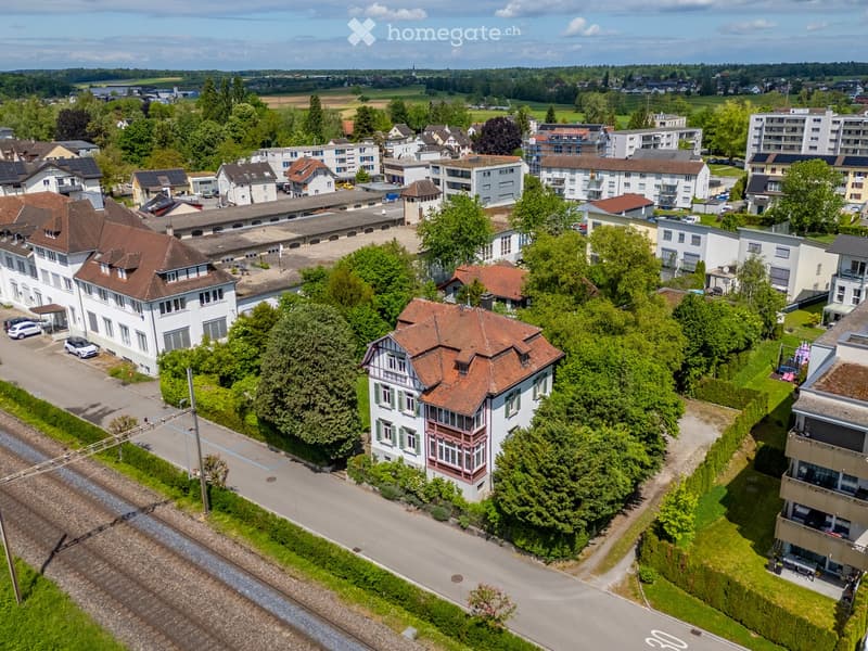 Aerial view of a residential area with multiple houses, trees, and a railway track running through the neighborhood.