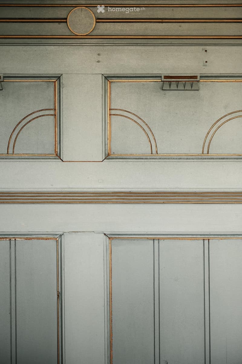 Close-up of a hallway with grey walls and decorative wooden trim featuring arched designs and a circular medallion above the door frame.