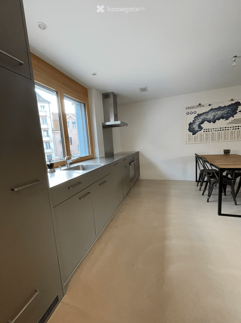 Modern kitchen with grey cabinets, a sink, and a small dining area with a table and chairs.