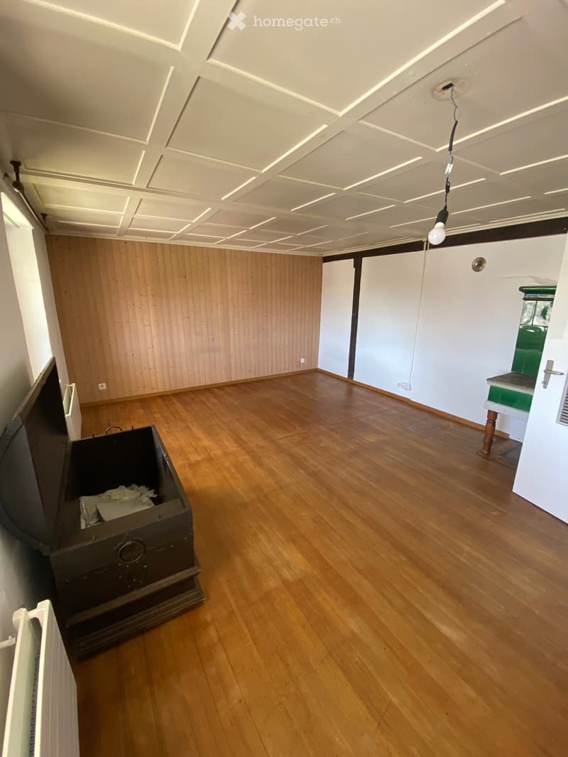 Empty room with wooden flooring, white walls, and a decorative ceiling. There is a small green cabinet and a black chest in the room.