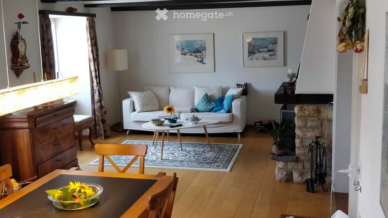 Cozy living room with a white sofa, coffee table, wooden dining table, fireplace, and decorative items.