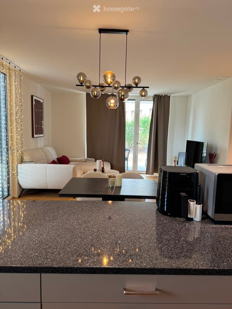 Modern open-plan living and dining area with a white sofa, dining table, chairs, coffee maker, microwave, and decorative candles.