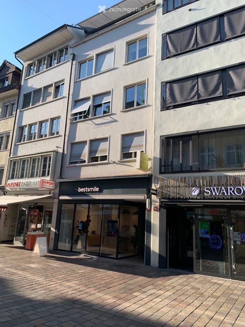Multi-story commercial building with large glass storefronts, including 'bestsmile' and 'SWAROVSKI' signage, and a brick-paved sidewalk.